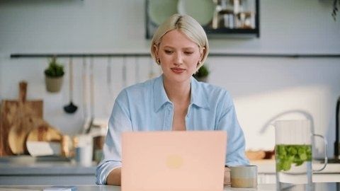 Kvinna skriver på en rosa laptop vid köksbordet